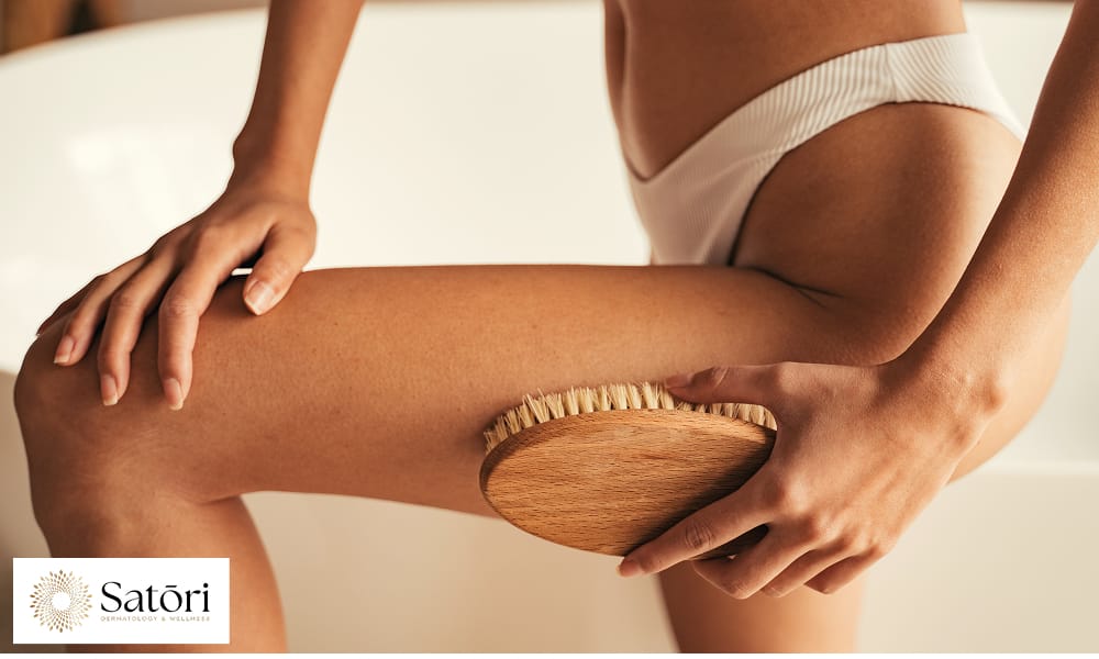 Woman sitting in a bathtub gently scrubbing her leg with an exfoliating brush.